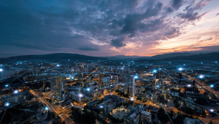 An overhead shot reveals a cityscape illuminated at dusk, showcasing numerous buildings and structures. The image captures a network of connected lights spanning across the city. The sky presents a dramatic blend of colors, suggesting a transition between day and night. This view could be used in various commercial or editorial projects.の素材