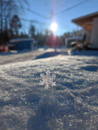 A detailed image captures a delicate snowflake resting on a snowy surface, with the sun shining brightly in the background. The photograph showcases the intricate structure of the ice crystal, emphasizing its translucent quality. This scene evokes a wintery atmosphere, suitable for various editorial and commercial applications.の素材