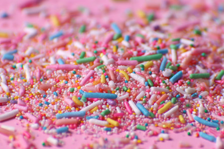 This image showcases a close-up of a vibrant assortment of sprinkles scattered across a pink surface. The composition highlights a mix of colors, textures, and shapes. This visual could be utilized for various commercial purposes, including culinary projects, food-related marketing, and design elements.の素材
