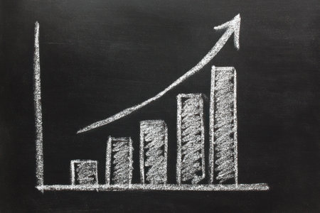 A chalk-drawn graph depicts an upward trend on a dark background, showcasing financial progress. The image features a bar chart with increasing columns and a line indicating growth. The style suggests a concept of business, finance, and positive development. Suitable for commercial and editorial applications, illustrating concepts of success.の素材