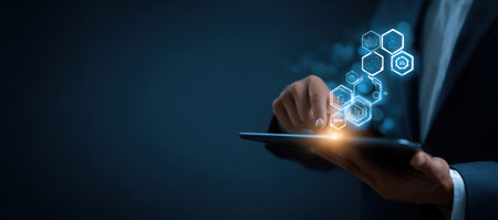 A person holds a tablet with glowing digital hexagonal elements. The image features a dark background with blue and orange highlights. It suggests a technological or business setting, potentially for use in marketing, design, or presentations. The overall style is modern and professional.の素材
