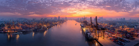 An aerial view presents a city landscape at dusk, featuring a river and illuminated harbor structures. The sky displays a gradient of colors from orange to purple, casting warm light. Buildings line the horizon, with lights creating a textured effect. This image could be used for illustrating urban development or commercial concepts.の素材