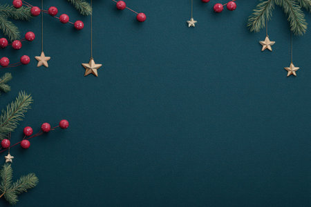 A festive arrangement features evergreen branches, red berries, and gold star ornaments suspended against a deep teal backdrop. The composition is overhead with balanced elements creating a visual space. This image could be suitable for holiday-themed marketing materials or editorial content.の素材