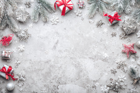 An overhead shot showcases a winter holiday arrangement with various decorative elements. Presents tied with red bows and glittering ornaments are scattered among frosted evergreen branches. The composition exhibits a bright, soft lighting and textured surface, suitable for seasonal projects or design applications.の素材