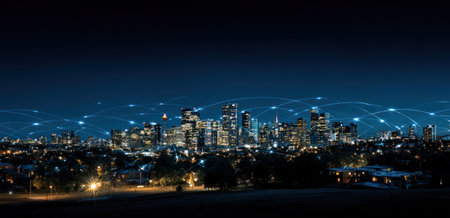 An aerial perspective showcases a cityscape illuminated at night. Buildings are silhouetted against a dark blue sky, with connected lines suggesting data transmission. The image displays a modern urban setting. It is potentially suitable for use in concepts of technology, infrastructure, and communication.の素材