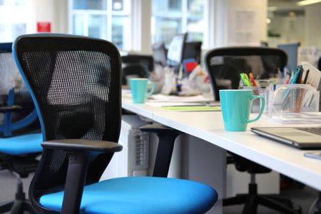 An office interior showcases multiple workstations with chairs and desks. The image highlights a bright, well-lit environment, possibly day, with a focus on workspace organization. The scene presents a clean design with ergonomic chairs, ideal for use in commercial projects promoting modern office environments or business-related themes.の素材