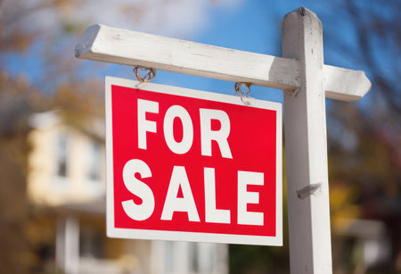 A red and white 'FOR SALE' sign is displayed on a wooden post against a blurred background, suggesting a real estate context. The image showcases a sign with bold lettering, likely used to promote property availability. The composition implies an outdoor setting, potentially for commercial applications.の素材