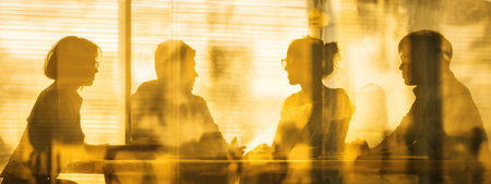 A group of people are silhouetted, engaged in a discussion. The warm lighting creates a golden hue throughout the composition. The style suggests a focused conversation happening indoors. The image could be used for business, communication, or teamwork-related articles.の素材