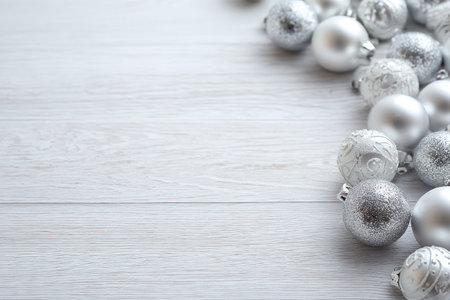 Numerous silver ornaments are arranged on a pale wooden surface. The composition showcases various textures and reflective qualities. The soft lighting highlights the round shapes and creates a festive ambiance. Suitable for holiday-themed advertising, design projects, and visual content creation.の素材