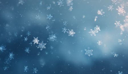 Numerous detailed snowflakes are captured against a soft, blurred blue backdrop. The image showcases a sense of movement with some snowflakes in focus, while others gently fade out of view. The composition utilizes a shallow depth of field, enhancing the visual interest suitable for creative or seasonal content.の素材