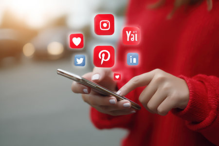 A person is interacting with a smartphone, with several social media icons floating in the air. The image showcases the user's hand and phone, with colorful icons representing various online platforms. The composition uses a shallow depth of field, with soft lighting and a blurred background, and it could be used for articles, advertising, or marketing.の素材