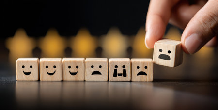 A hand manipulates a wooden block with a sad face among other blocks displaying various emotions. The image features a close-up perspective, with a shallow depth of field, highlighting the textures of the wooden cubes. The lighting is soft, and the composition focuses on the concept of emotion. Suitable for illustrating psychology, communication, or marketing.の素材