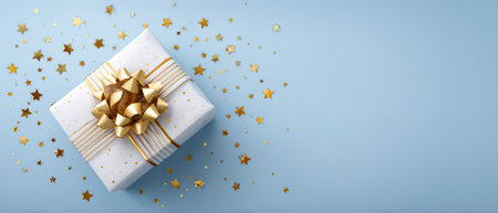 A present, wrapped with a white paper and decorated with gold ribbon and bow, rests on a light blue surface. Golden star-shaped confetti surrounds the gift. This composition features soft lighting and could be used for festive, holiday, or celebratory content. The image provides space for various commercial or editorial applications.の素材