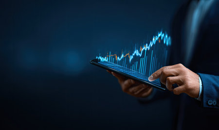 An individual in a professional setting examines a digital financial chart displayed on a tablet. The image showcases a dark backdrop, emphasizing the glowing lines representing market trends. It suggests a focus on business analysis and could be used in various commercial or editorial contexts related to finance or technology.の素材