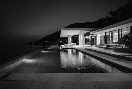 A grayscale image showcases a contemporary home with an infinity pool reflecting the building's lights. The composition highlights geometric lines and the play of light and shadow, featuring a sleek, minimalist design. This image could be suitable for architectural, travel, or lifestyle publications and commercial projects.の素材