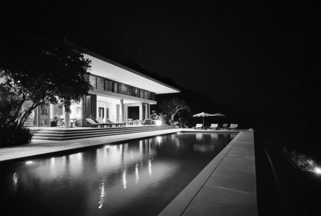 A grayscale photograph captures a modern home with a swimming pool under the night sky. The composition emphasizes architectural lines and reflections in the water. The image features high contrast, suggesting a luxury setting. Suitable for real estate, travel, or lifestyle publications and advertisements.の素材