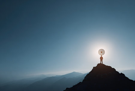 A silhouette of a person stands atop a mountain, holding a target symbol towards a bright, overhead light. The scene showcases cool blue tones with the silhouette in contrast. The image evokes concepts like achievement and focus, suitable for various business and inspirational projects.の素材