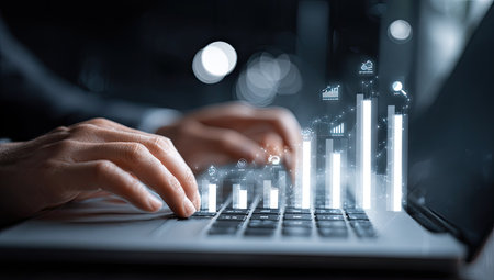 A person is shown using a laptop, with illuminated digital graphs and charts superimposed over the keyboard. The image displays a shallow depth of field, with soft lighting enhancing the visual data. It suggests a focus on business analytics, finance, or technology, and is suitable for various commercial applications.の素材