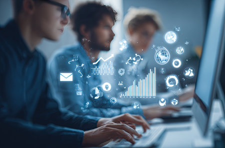 A diverse team of people is shown working in an indoor setting, likely an office environment. They are focused on computer screens, with projected digital icons and graphics overlaying the scene. The image suggests technological workflows, data analysis, and collaboration, suitable for various business and commercial applications.の素材