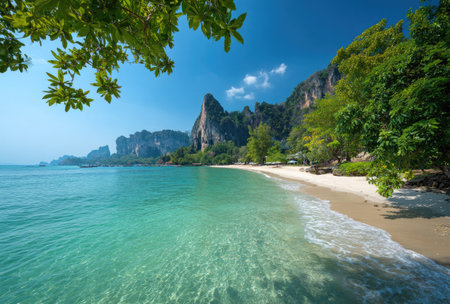 A stunning tropical beach scene with crystal-clear turquoise water meets a sandy shore. Lush green foliage frames the scene, while rocky mountains rise in the distance against a vibrant blue sky. This image is suitable for various commercial purposes, including travel and environmental themes.の素材