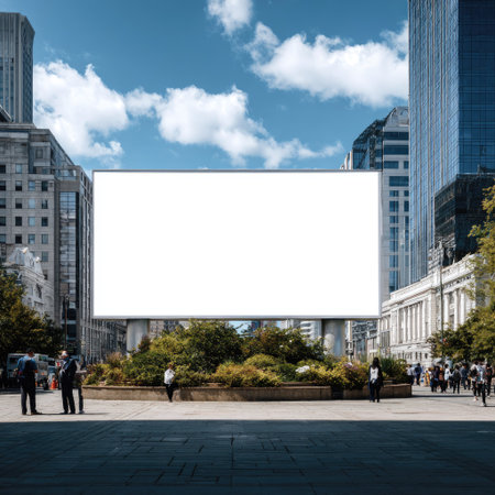 An outdoor billboard stands in an urban environment. The blank display is surrounded by trees and buildings, set against a backdrop of blue sky and clouds. The composition features a clear, wide view with natural lighting. This image could be used for advertising, marketing campaigns, or editorial purposes.の素材
