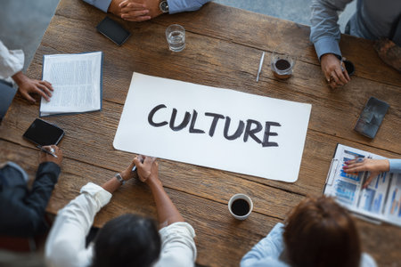 An overhead shot shows a group of people at a wooden table. A paper with the word "CULTURE" on it is in the center. The scene is brightly lit, suggesting a daytime meeting. The composition and style suggest it could be used for various business, communication, and educational purposes.の素材