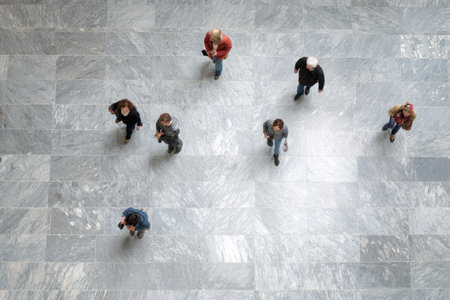 An aerial perspective showcases several individuals walking on a large, patterned surface. The composition uses a high angle, highlighting the arrangement of people. The scene, possibly indoors, features neutral colors and uniform lighting. This image could serve various commercial or illustrative purposes.の素材