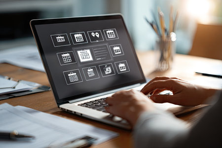 A person's hands work on a laptop, revealing calendar application icons on the screen. The scene, shot in close-up, displays soft lighting over a wooden table, suggesting an indoor setting. Potential uses include web design, technology, or business related projects.  The composition emphasizes technology and its applications.の素材