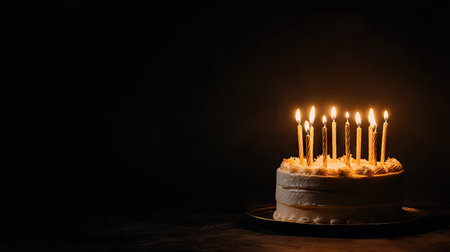 A birthday cake sits prominently, adorned with lit candles, against a dark backdrop. The composition highlights the warm glow of the flames against the contrasting darkness. This image suggests a festive occasion, suitable for various editorial and commercial applications. The scene employs selective lighting to draw the eye to the cake.の素材