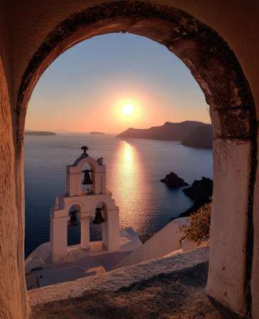 An arch frames a picturesque sunset over the ocean, highlighting a white church with bells. The image features warm colors and soft lighting, creating a tranquil atmosphere. The scene suggests a coastal environment during golden hour. Suitable for travel, tourism, or scenic visuals.の素材