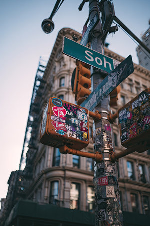 An upward perspective of a street corner features a metal pole supporting traffic lights and street signs. The scene showcases a building facade under a clear sky. The colors include browns, yellows, and blues, with a vintage aesthetic. This image would be suitable for commercial use.の素材