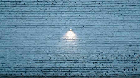 A close-up view presents a textured brick wall bathed in soft light. The wall exhibits a weathered appearance with visible imperfections. A single overhead light casts a warm glow, creating subtle shadows and highlights. This image can be used for design, advertising or as a textured backdrop.の素材