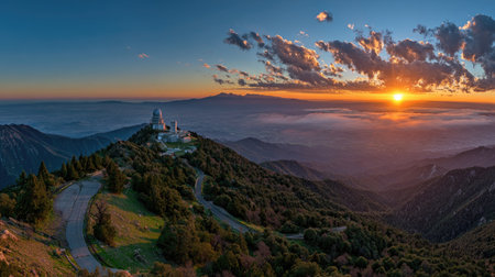 An observatory sits atop a tree-covered mountain under a sky painted with sunset hues. The scene features a winding road, and the lighting bathes the landscape in a golden glow. This image's visual appeal makes it suitable for use in travel, landscape, and scientific articles, as well as general editorial and commercial applications.の素材
