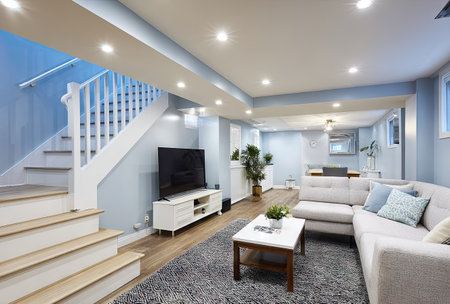 This interior photograph presents a modern living room featuring a staircase, television, and comfortable couch arrangement. The room's color scheme is light blue and white. The composition uses overhead lighting. The scene would be suitable for commercial and editorial uses. It emphasizes contemporary design.の素材