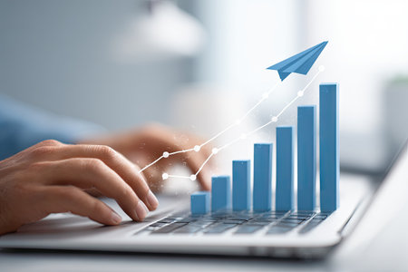 A person's hands work on a laptop, overlaid with a graphic of an increasing bar chart and paper airplane. The image features a bright, clean look with soft focus, highlighting a digital concept with a modern business aesthetic. Suitable for presentations and marketing materials.の素材