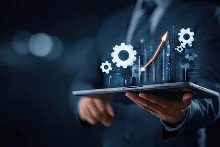 A person in a suit is holding a tablet displaying digital gears and a rising graph, indicating growth. The image utilizes a dark background and blue tones, with glowing elements suggesting a technology or business theme. Suitable for illustrating business strategy or technological advancement.の素材