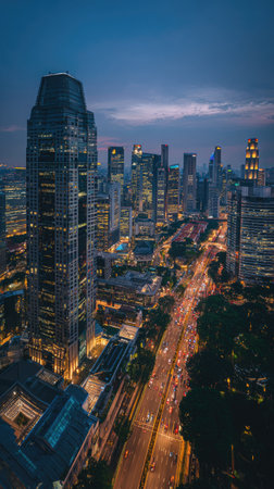 An elevated view captures a cityscape as twilight descends, showcasing numerous tall buildings. Structures display various architectural designs and are lit by artificial lights. The image presents a blend of cool and warm colors. This scene could be suitable for diverse commercial applications.の素材