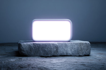 An illuminated rectangular object rests on a textured stone block against a neutral backdrop. The object emits a bright white light framed by a soft, glowing border. The image showcases a minimalist composition with subtle shadows, ideal for digital design and conceptual applications. It's suitable for various commercial purposes.の素材