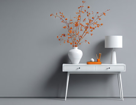 A minimalist interior scene depicts a white table adorned with a white vase holding orange branches and a white lamp. The composition features clean lines and a modern aesthetic with a gray backdrop. This image highlights contrasting colors and textures, suitable for design and lifestyle publications or commercial applications.の素材