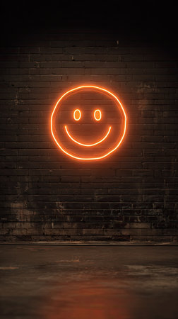 A glowing neon smiley face illuminates a weathered brick wall, creating a striking contrast. The image showcases warm orange hues and a sleek, modern style. The composition suggests an urban setting with a dim atmosphere, suitable for various editorial and commercial applications. The design is presented against a textured background.の素材