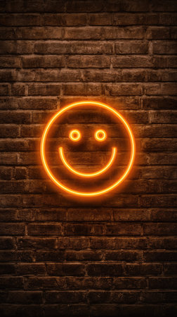A glowing neon smiley face illuminates against a textured brick wall. The image showcases warm orange hues, creating a vibrant visual contrast. The close-up composition highlights the simple yet effective design, suitable for various editorial and commercial applications. The scene implies an indoor setting with artificial lighting.の素材