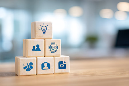 A close-up captures a stack of wooden blocks featuring various blue icons. The blocks are arranged on a wooden surface, with a blurred office environment in the background. The lighting is soft and natural, highlighting the textures of the wood. This image may be suitable for illustrating business, technology, or creative concepts.の素材