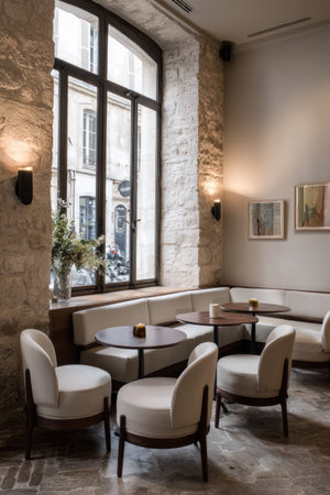 This interior showcases a stylish arrangement with comfortable chairs and small tables. Warm lighting illuminates the scene, highlighting the textures of the stone walls and neutral color palette. A large window provides an outside view. This image is suitable for commercial use, offering a glimpse into a modern, inviting space.の素材