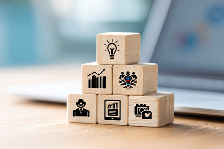 A pyramid of wooden blocks displays various business icons. The blocks have a natural wood texture with black symbols. The composition features a shallow depth of field, with a blurred background. This image is suitable for illustrating concepts of business, innovation, and teamwork, and is appropriate for commercial and editorial purposes.の素材