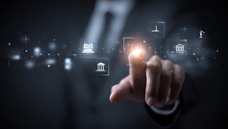 A person's finger touches a glowing digital interface showcasing various icons. The composition presents a dark, professional setting with overhead lighting. The visual elements suggest a focus on technology, finance, and business operations. This image is suitable for illustrating concepts in technology, business, and data analysis.の素材