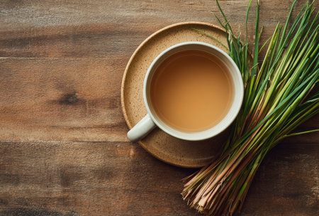 An overhead shot presents a cup of tea resting on a plate, alongside a bundle of lemongrass. The arrangement, set on a wooden surface, creates a natural aesthetic. The composition uses warm tones and lighting. Suitable for use in projects about food, beverages, or wellness.の素材