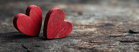 Two heart-shaped objects, painted red, rest on a rustic wooden surface. The composition highlights the contrasting textures of the smooth hearts against the rough wood. The lighting appears soft, creating gentle shadows. Suitable for various applications, including design projects, and visual content.の素材