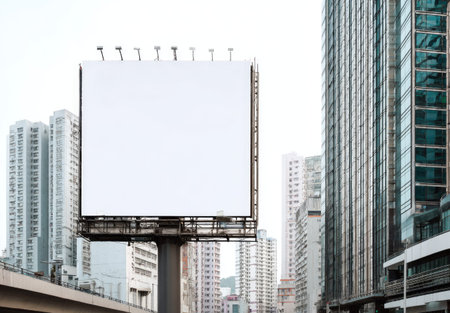A large blank billboard stands prominently against a backdrop of towering buildings, offering copy space. The composition features an overhead perspective with diffused lighting. This image is suitable for commercial applications related to advertising, marketing, and visual communication, with a focus on delivering messages.の素材