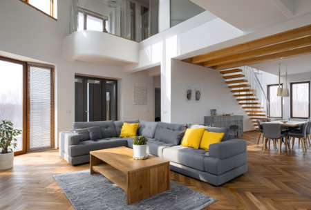 A spacious living room is showcased with a large gray sofa accented by yellow cushions. A wooden coffee table rests on a gray rug, complemented by a hardwood floor and natural lighting from large windows. The interior setting suggests a comfortable residential space, suitable for various editorial and promotional purposes.の素材