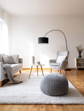 A well-lit interior showcases modern furniture arranged on a white rug and wooden floor. A grey sofa, armchair, and footstool, alongside a round table and a tall lamp create a comfortable ambiance. The composition, lit by natural light, suits various commercial or editorial applications, offering a clean, contemporary aesthetic.の素材